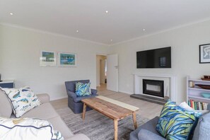 A living room with a sofa, armchair, coffee table, fireplace, TV, and framed pictures on the wall. - Mooinooientjie | Voelklip beaches | Hot tub (Hermanus)