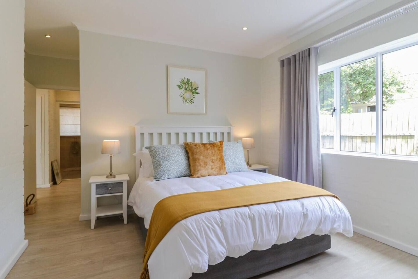 A bedroom with a bed, bedside tables, a window with curtains, and a door leading to another room.