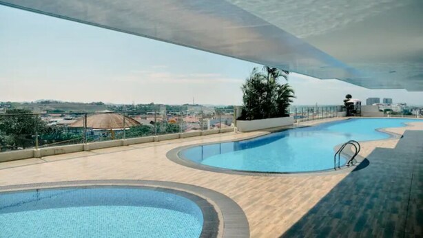 Una piscina en la azotea con diseño curvo, rodeada por una terraza de madera y una barandilla de cristal.
