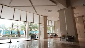 Un vestíbulo espacioso con amplias puertas de vidrio, piso pulido y una zona de estar con algunas sillas.