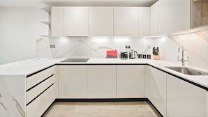 Una cocina moderna con armarios blancos, encimera de mármol y un lavamanos empotrado.