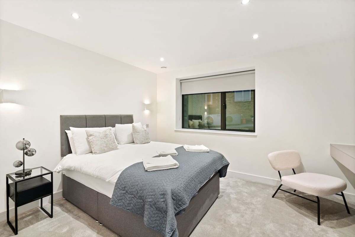 A modern bedroom with a large bed, bedside lamps, a chair, and a window with a view.