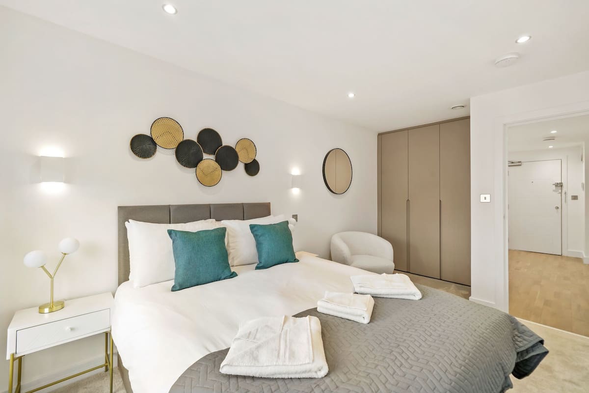 A modern bedroom with a large bed, bedside tables, a mirror, and a wardrobe.