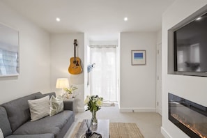 A living room with a grey sofa, a coffee table, a guitar, a fireplace, and a door leading to another room. - Modern Flat Minutes from Exmouth Sea Front (Exmouth)