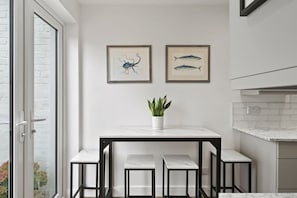 A modern kitchen with a white marble countertop, black metal stools, and two framed fish illustrations on the wall. - Modern Flat Minutes from Exmouth Sea Front (Exmouth)