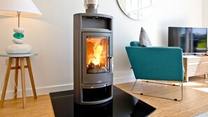 A modern living room with a wood-burning stove, a teal chair, a wooden side table with a lamp, and a flat-screen TV. - 2 bedroom accommodation in Carbis Bay, near St Ives (Carbis Bay, near St Ives)