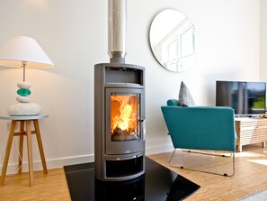 A modern living room with a wood-burning stove, a teal chair, a wooden side table with a lamp, and a flat-screen TV. - 2 bedroom accommodation in Carbis Bay, near St Ives (Carbis Bay, near St Ives)