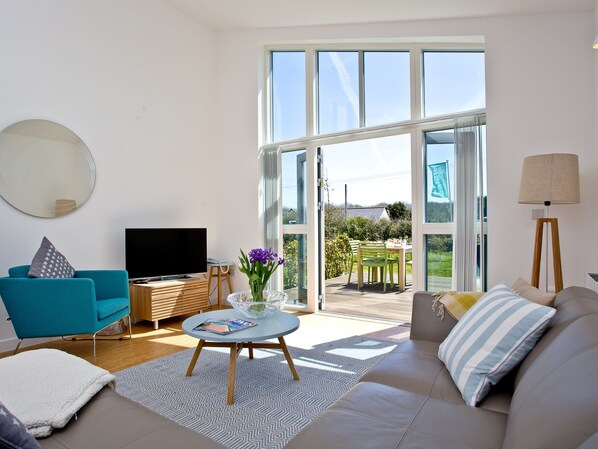 A modern living room with a sofa, a television, a coffee table, and a dining area with chairs.