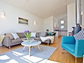 A modern living room with a sofa, a blue armchair, a coffee table with a vase of flowers, and a kitchen in the background. - 2 bedroom accommodation in Carbis Bay, near St Ives (Carbis Bay, near St Ives)