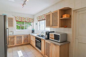 Cozinha com armários de madeira, micro-ondas, fogão e janela com vista para o verde.