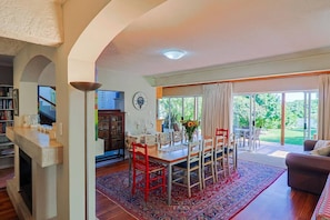A spacious living area with a dining table, red chairs, a fireplace, and a large window with a view of greenery.
