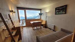 A cozy room with a wooden dining table, a sofa, and a large window offering a mountain view. - 10m from ski slopes, view mountain, balcony, tv, 26m², La Plagne (Aime)