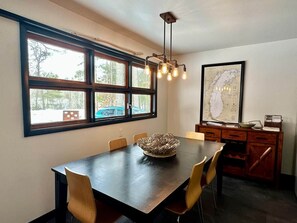 Un coin repas avec une table en bois foncé, six chaises, un centre de table décoratif en forme de bol et un luminaire suspendu.