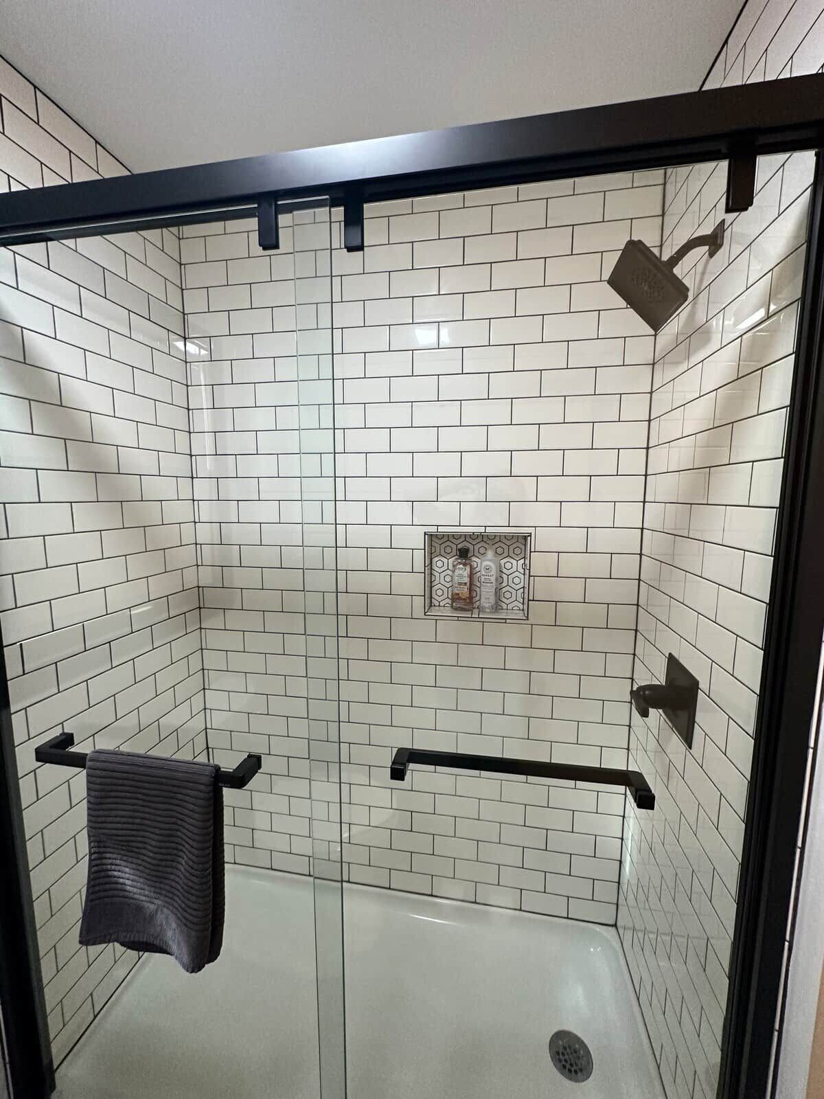 A shower with white subway tiles, a glass door, and a towel rack.