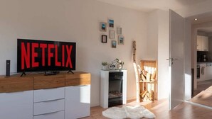 Una sala moderna con un televisor de pantalla plana grande, un mueble de madera, una mesita con una bicicleta y plantas, y una alfombra de piel blanca en el suelo.