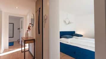 Un dormitorio con cama azul, ropa de cama blanca y una lámpara de pared.