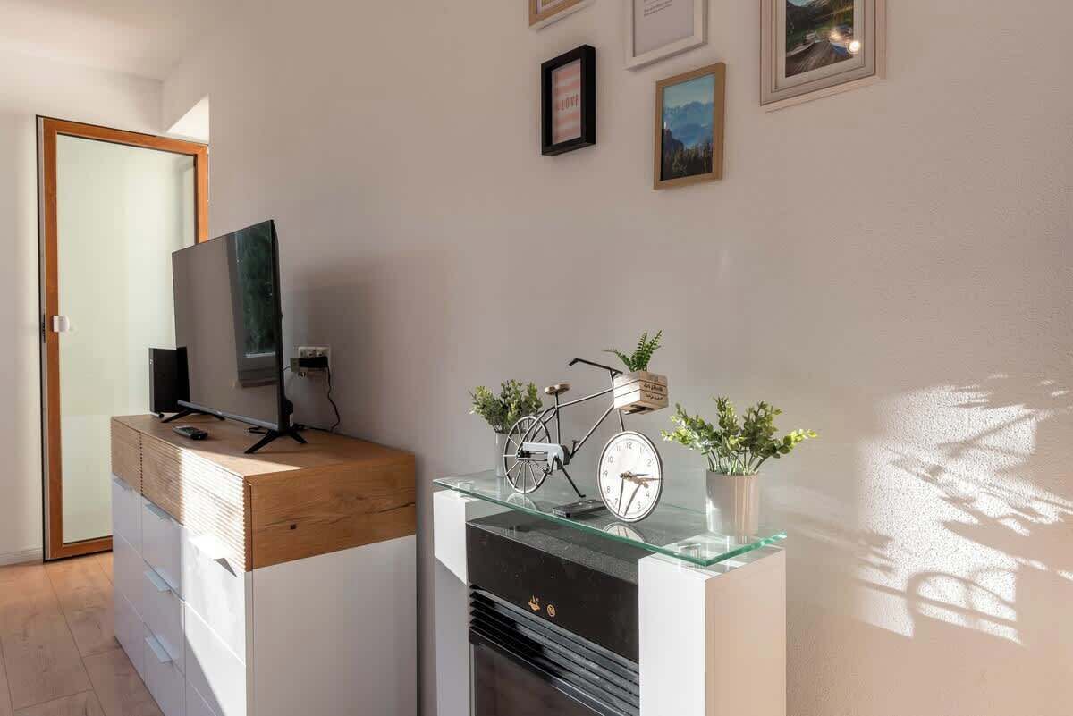 Un salon moderne avec un bureau en bois, une télévision, un vélo et une horloge posée sur une étagère en verre.