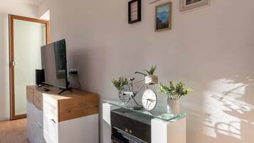 Un salon moderne avec un bureau en bois, une télévision, un vélo et une horloge posée sur une étagère en verre.