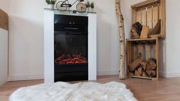 Un salon moderne avec une cheminée, un tapis blanc et moelleux, une étagère en bois avec des bûches et un vélo posé sur une étagère en verre au-dessus de la cheminée.