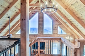 Experience the rustic charm of this attic room with a high ceiling, exposed beams, and a skylight offering a view of the surrounding landscape.