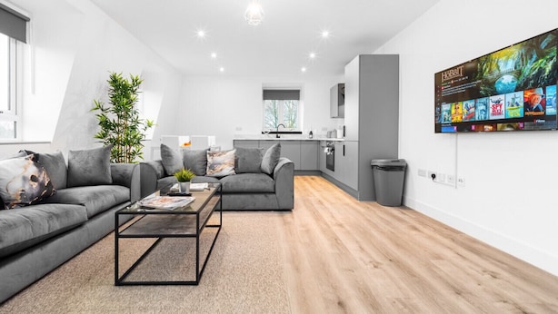 Una sala de estar moderna con un sofá gris, una mesa de centro y un televisor en la pared mostrando opciones de películas.