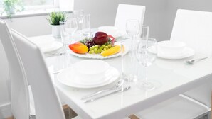 Una mesa de comedor dispuesta con platos blancos, vasos transparentes y una composición de frutas.