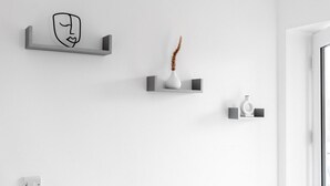 Un baño minimalista con paredes blancas, un perchero para toallas, un jarrón con plantas secas y un dispensador de jabón.