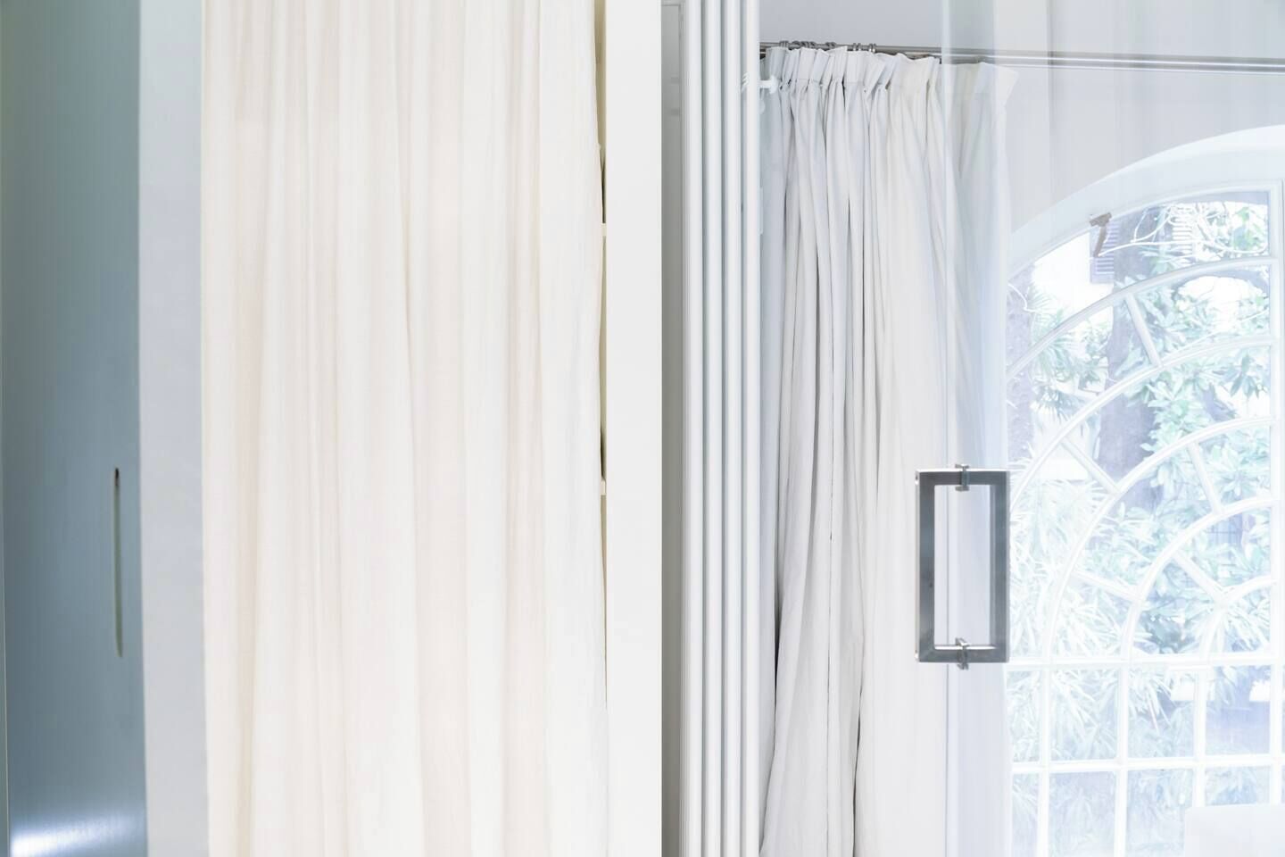 A room with a large window, white curtains, and a metal handle on the window.