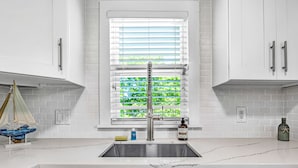 A kitchen with white cabinets, a marble countertop, a stainless steel sink, a window with blinds, and a small sailboat decoration. -  Bungalow #3 - 2 Bed/1 Bath & Pool in Islamorada (Islamorada)