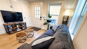 Una sala de estar con sofá, mesa de centro, televisor, estantería y un amplio ventanal.