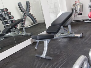 A gym with a bench, dumbbells, and a mirror.