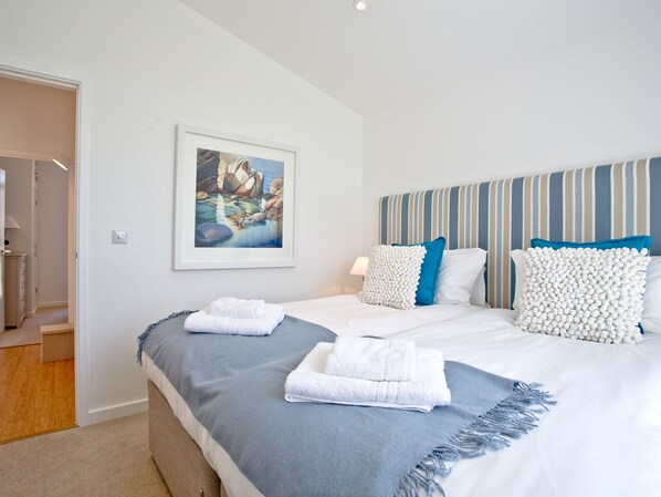 A hotel room with a large bed, a headboard with stripes, a framed picture on the wall, and a door leading to another room.