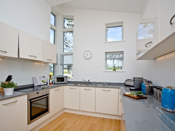 A modern kitchen with white cabinets, a microwave, a sink, and a clock on the wall.