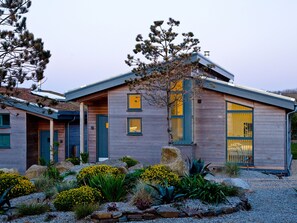 A modern house with a sloped roof, multiple windows, and a well-maintained garden with various plants and rocks.