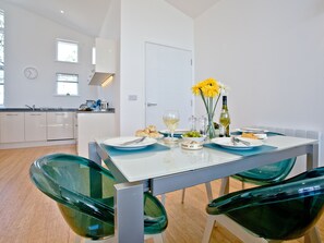 A modern kitchen with white cabinets, a dining table with blue placemats, and green chairs.