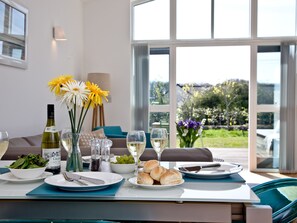 A dining table set with plates, glasses, and a bottle of wine, with a view of greenery outside.