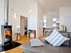 A modern living room with a wood-burning stove, a sofa with striped pillows, a small table with a lamp, and a bookshelf. - 2 bedroom accommodation in Carbis Bay, near St Ives (Carbis Bay, near St Ives)
