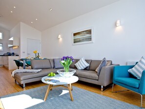 A modern living room with a sofa, armchair, coffee table, and a painting on the wall.