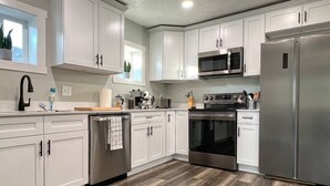 A modern kitchen with white cabinets, stainless steel appliances, and a wooden floor.
