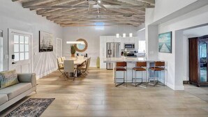 A spacious living area with a high ceiling, a dining table with chairs, a kitchen area with bar stools, and a large window. - Oasis Retreat! - 4BR/3BA Private Pool Home! (Fort Lauderdale)