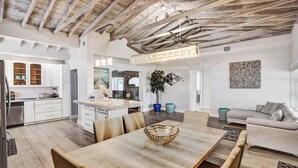 A spacious living area with a high ceiling, a dining table with chairs, a sofa, and a kitchen in the background. - Oasis Retreat! - 4BR/3BA Private Pool Home! (Fort Lauderdale)