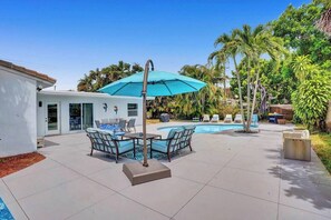 A poolside area with a table and chairs, a covered umbrella, and a pool.