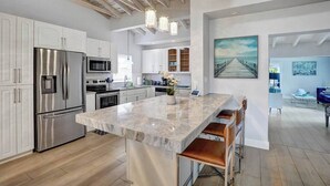 A modern kitchen with stainless steel appliances, a marble island, and a dining area with bar stools. - Oasis Retreat! - 4BR/3BA Private Pool Home! (Fort Lauderdale)