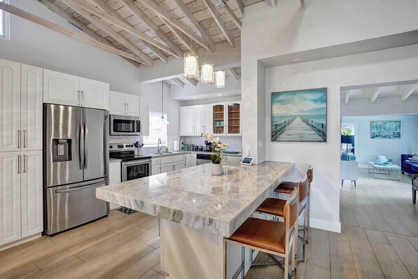 A modern kitchen with stainless steel appliances, a marble island, and a dining area with bar stools.