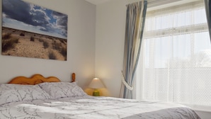 A bedroom with a bed, a lamp, a window with curtains, and a painting on the wall. - A wonderful chalet set in a great seaside location. (Kessingland)