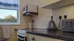 A kitchen with a stove, oven, microwave, toaster, and a window with a view of boats. - A wonderful chalet set in a great seaside location. (Kessingland)