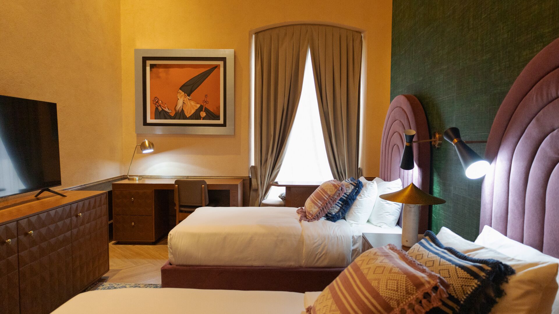 Una habitación de hotel con cama, mesita de noche, lámpara, televisión y un cuadro en la pared.