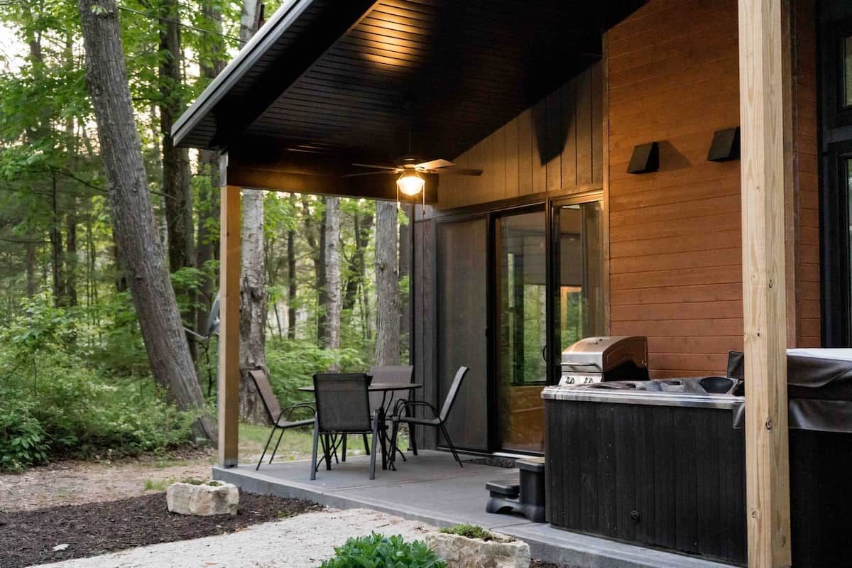 A wooden cabin with a covered patio, outdoor seating, and a grill.