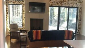 A living room with a fireplace, a sofa, and a dining area. - ~Driftwood Haven Cottage  (Two Rivers)