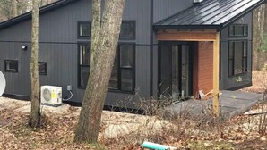 A modern, dark-colored building with multiple windows and a small wooden door. - ~Driftwood Haven Cottage  (Two Rivers)